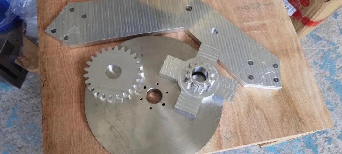 Machined flywheel, gears, and mounting plates on a workbench.
